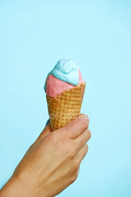 Жіноча рука тримає морозиво конус перед синім фоном. — стокове фото