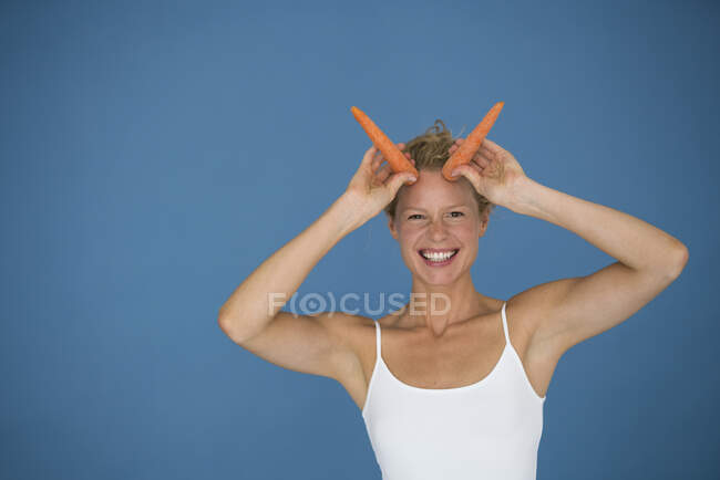 Улыбающаяся блондинка с морковкой на синем фоне — стоковое фото