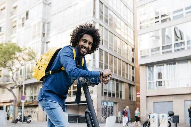 Портрет усміхненого молодого чоловіка з жовтим рюкзаком на E-Scooter в місті Барселона, Іспанія — стокове фото