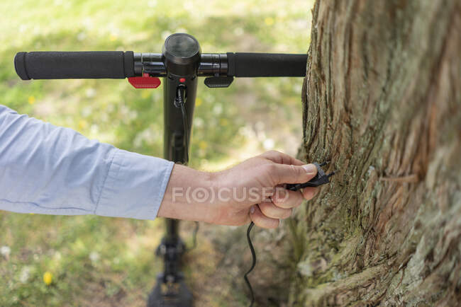 Tappo mano uomo di E-Scooter davanti al tronco d'albero, primo piano — Foto stock