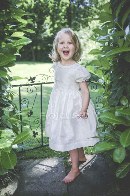 Retrato de menina feliz vestindo vestido branco em pé perto do portão do jardim — Fotografia de Stock