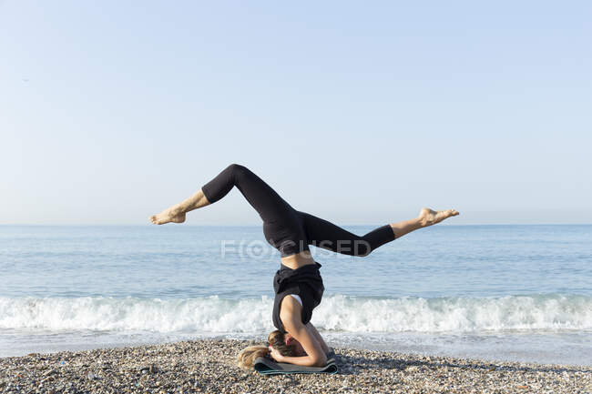 Молодая женщина практикует йогу на пляже, делает стойку на голове — стоковое фото
