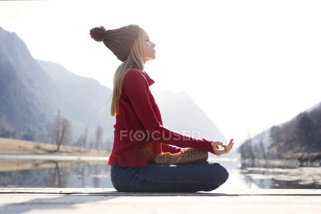 Young blond woman sitting on jetty at a lake in winter — Fotografia de Stock