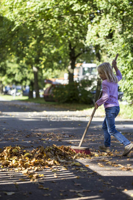 Ragazza spazzare foglie sul marciapiede — Foto stock