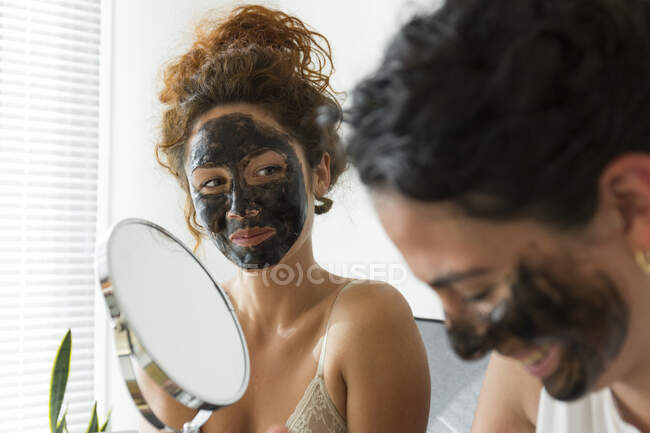 Dos jóvenes felices con máscaras faciales en casa - foto de stock