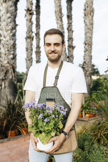 Portrait of a smiling worker in a garden center holding a lilac plant — Stock Photo