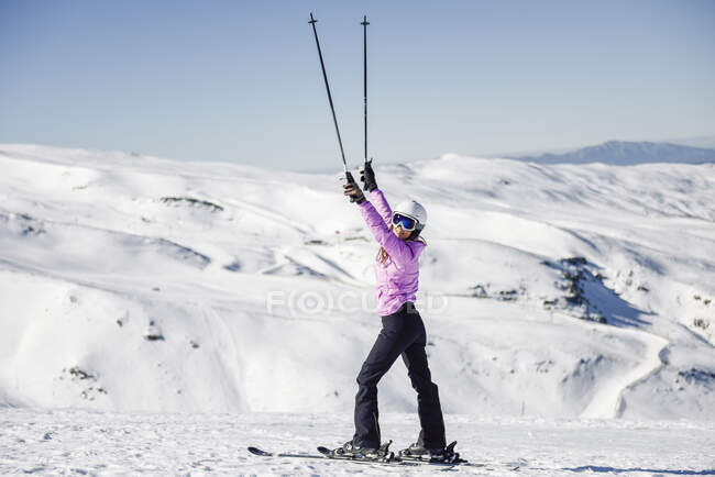 Mujer feliz levantando sus bastones en un paisaje cubierto de nieve en Sierra Nevada, Andalucía, España - foto de stock