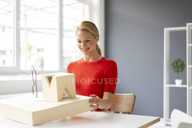 Jeune femme au bureau regardant le modèle architectural sur le bureau — Photo de stock