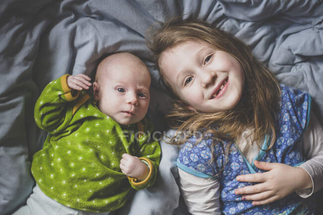 Portrait de petite fille souriante couchée sur le lit à côté de la petite fille, vue du dessus — Photo de stock