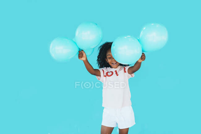 Menina na frente de uma parede azul, segurando balões — Fotografia de Stock