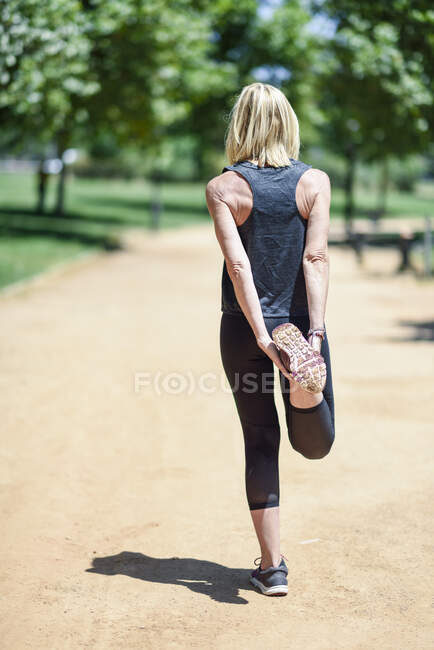 Mature woman stretching leg on a path in a park — Stock Photo