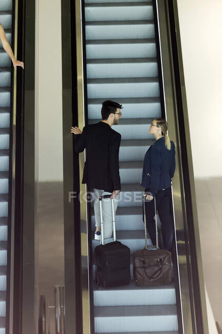 Deux jeunes partenaires d'affaires avec bagages parlant sur un escalier roulant — Photo de stock