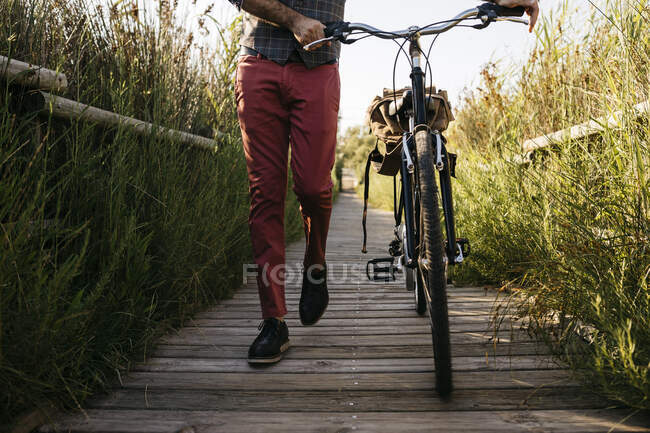 Well dressed man walking with his bike on a wooden walkway in the countryside after work — Stock Photo
