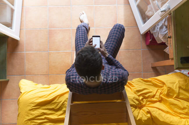 Homem usando smartphone, sentado em escada de madeira no quarto — Fotografia de Stock