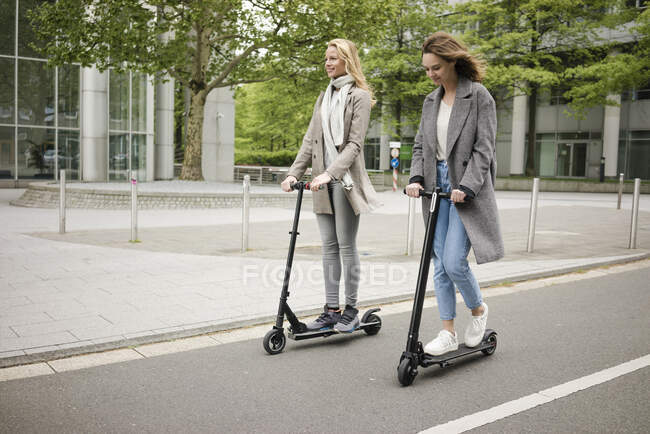 Молодые женщины ездят на электрических скутерах по улице — стоковое фото