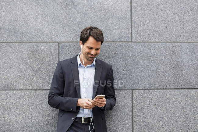 Smiling businessman with earphones looking at mobile phone — Stock Photo