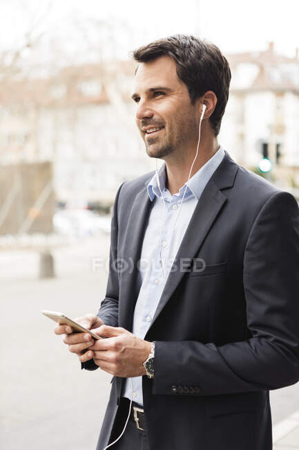 Portrait of businessman using mobile phone and earbuds in the city — Stock Photo