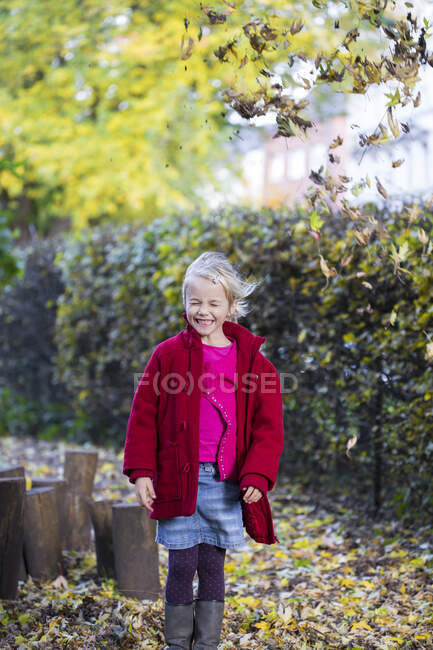 Ritratto di bambina sorridente che lancia foglie in aria in autunno — Foto stock