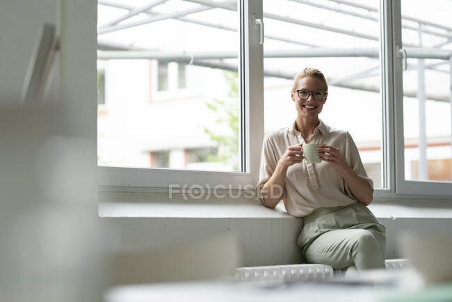 Porträt einer lächelnden jungen Geschäftsfrau mit einer Tasse Kaffee am Fenster — Stockfoto
