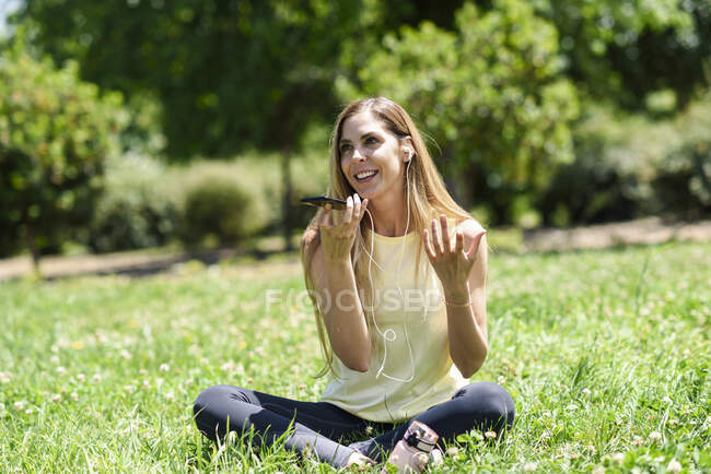 Donna che utilizza il suo smartphone, riposando nell'erba di un parco dopo l'esercizio fisico — Foto stock