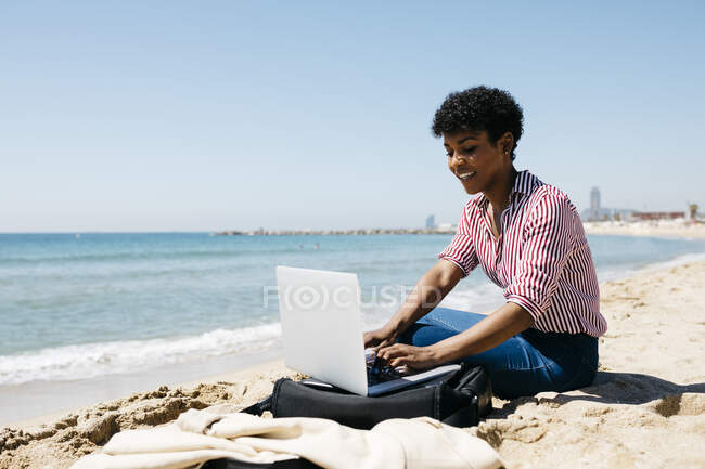 Frau sitzt am Strand während der Arbeit mit dem Laptop — Stockfoto