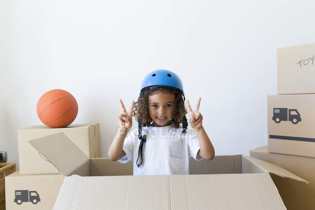 Портрет девушки в велосипедном шлеме, выглядывающей из картонной коробки в новом доме — стоковое фото