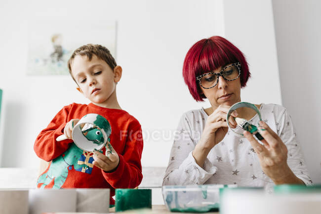 Mother and son doing crafts at home, painting cardboard rolls to make a Christmas tree — Stock Photo