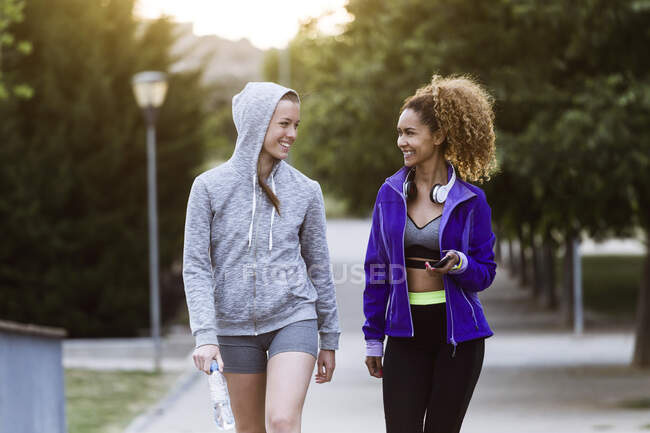 Due giovani donne sorridenti e sportive che camminano nel parco dopo l'allenamento — Foto stock