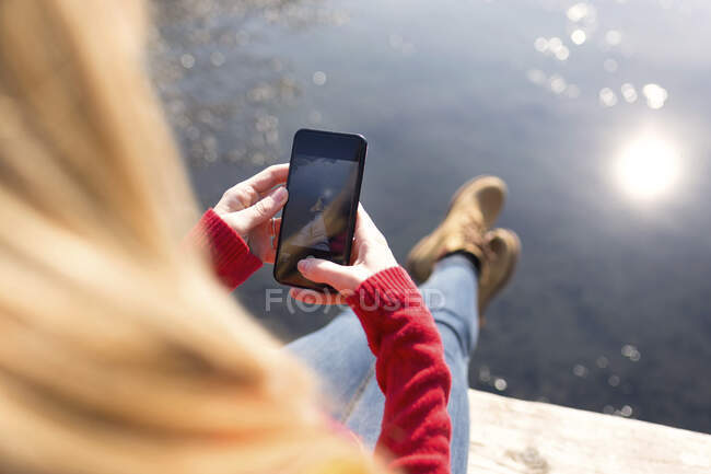 Young blond woman using smartphone at a lake in winter — Fotografia de Stock