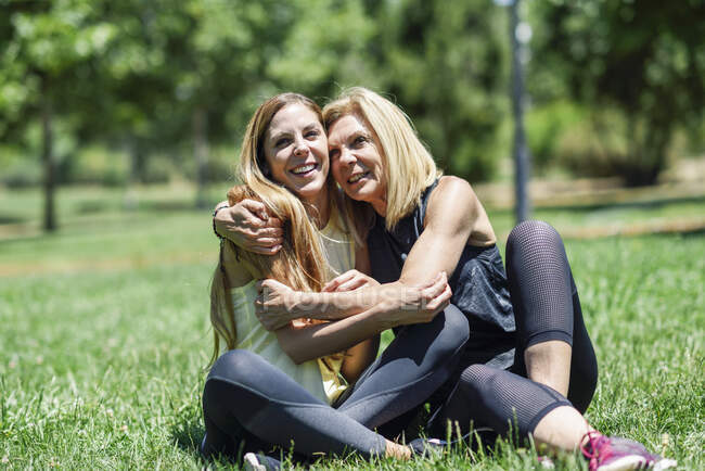 Спортивная зрелая женщина и ее дочь обнимаются на лугу в парке — стоковое фото