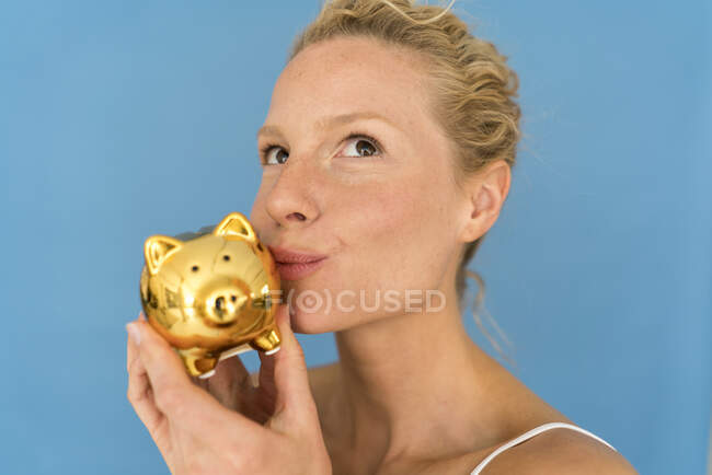 Retrato de una mujer rubia besándose en una alcancía dorada - foto de stock