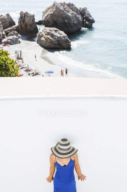 Mulher usando vestido azul e chapéu de palha em pé na frente da parede branca, Nerja, Espanha — Fotografia de Stock