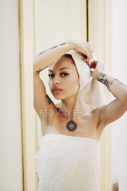 Portrait of tattooed woman at home with hair wrapped in a towel — Stock Photo