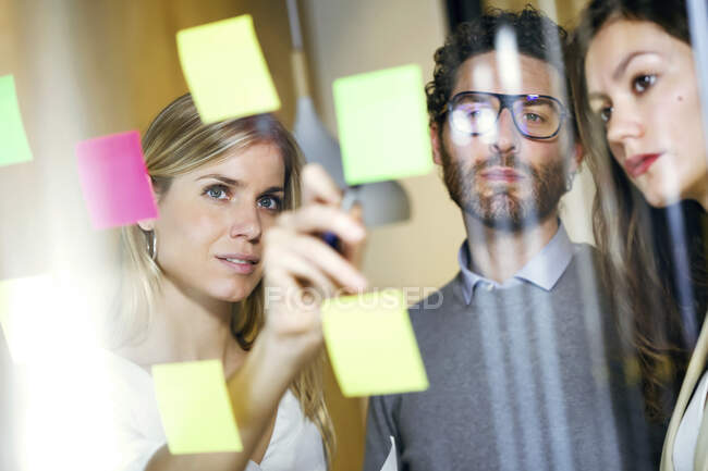 Drei Geschäftsleute beim Brainstorming mit klebrigen Zetteln an einer Glaswand — Stockfoto