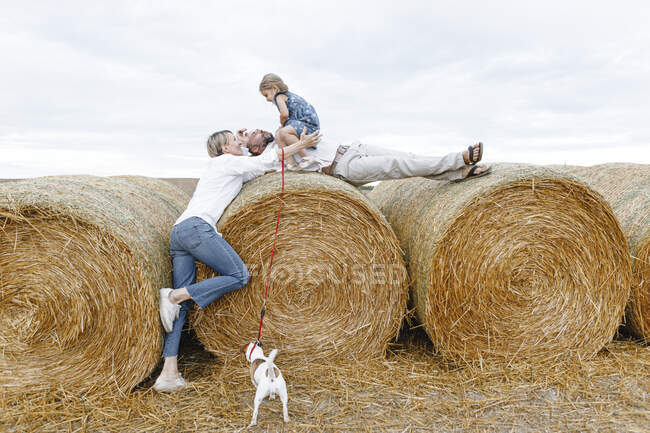 Famille heureuse avec chien embrassant sur balles de foin — Photo de stock