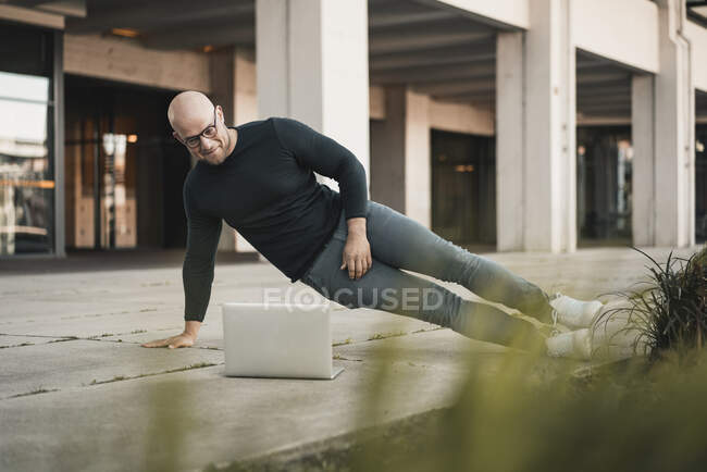Portrait d'un homme souriant faisant des pompes tout en regardant un ordinateur portable — Photo de stock