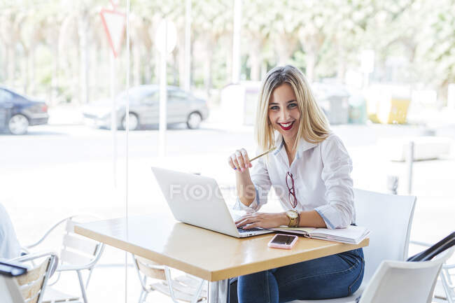 Портрет усмішки молодої жінки з ноутбуком на столі в кафе. — стокове фото