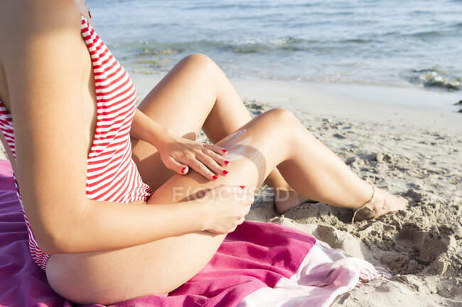 Женщина, сидящая на пляже, намазывающая кремом для загара — стоковое фото