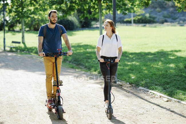 Pareja montando scooters eléctricos en un parque de la ciudad - foto de stock