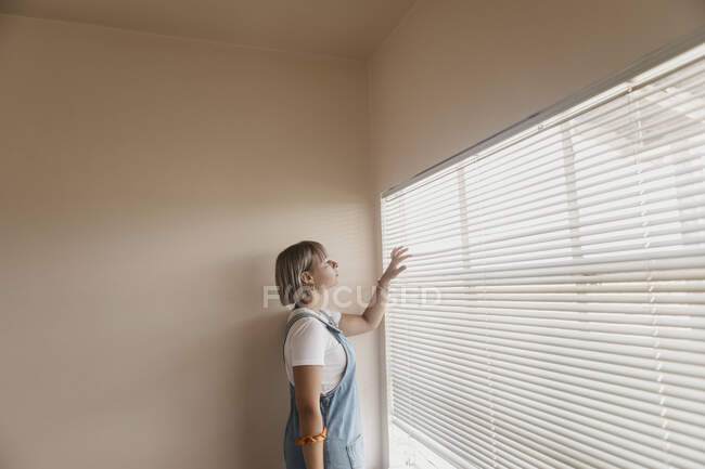 Giovane donna che guarda attraverso le tende alla finestra — Foto stock