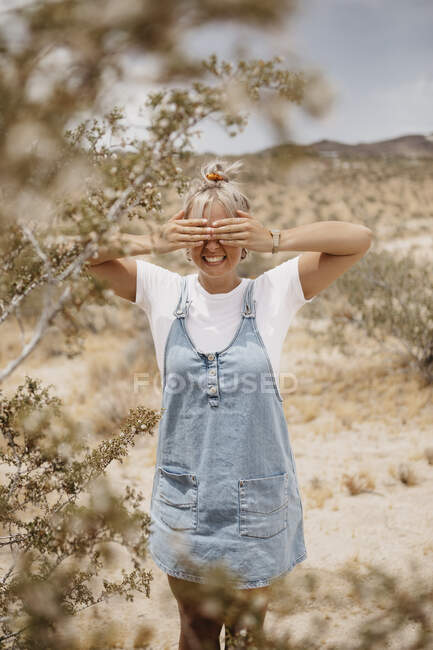 Mujer joven y feliz de pie en el paisaje del desierto que cubre sus ojos, Joshua Tree National Park, California, EE.UU. - foto de stock