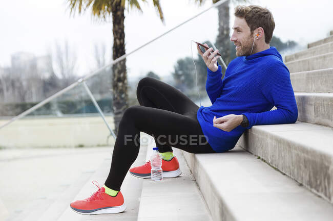 Jogger assis sur les marches parler sur un téléphone mobile avec les mains libres — Photo de stock