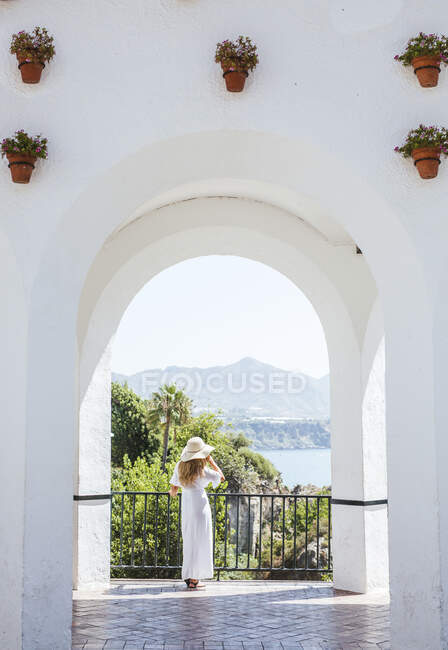 Back view of woman wearing white dress and straw hat looking at view, Nerja, Spain — Stock Photo