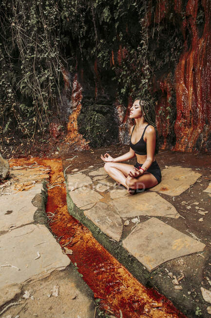 Junge Frau meditiert an einem Wasserfall — Stockfoto