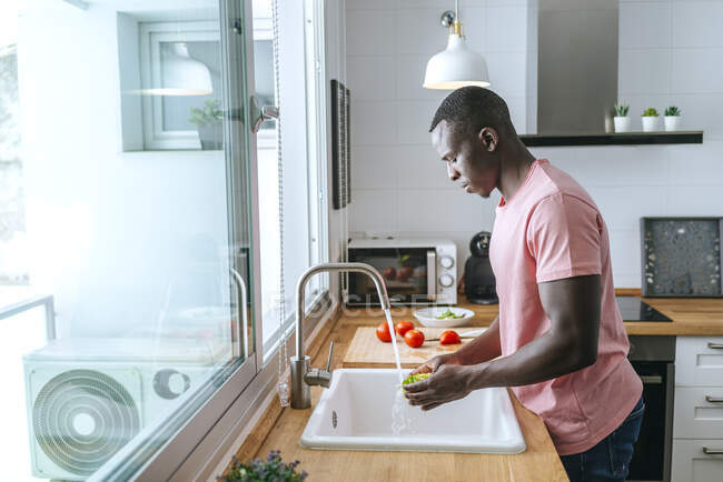 Молодой человек стирает салат на кухне — стоковое фото