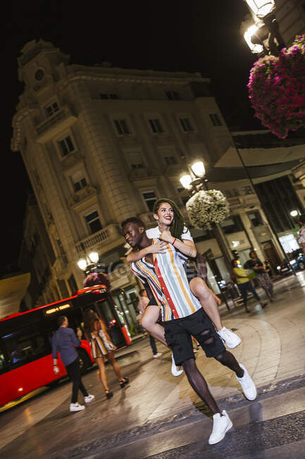 Junger Mann trägt Freundin nachts huckepack durch die Stadt — Stockfoto