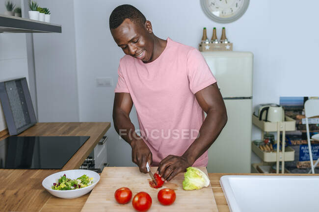 Giovane in cucina che taglia il pomodoro per un'insalata — Foto stock
