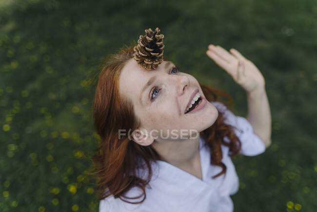 Mujer pelirroja balanceando un cono de pino en su frente - foto de stock