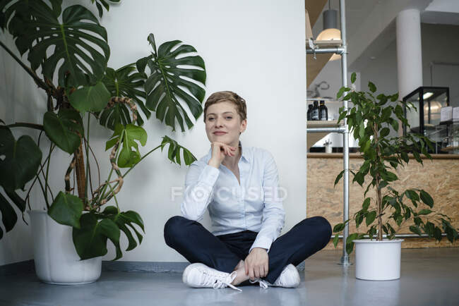 Retrato de uma mulher de negócios sentada no chão cercada por plantas — Fotografia de Stock