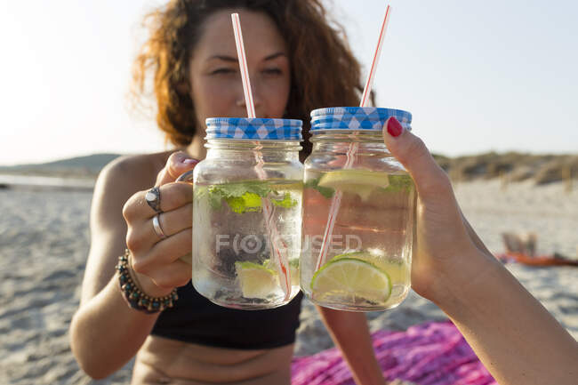 Due bicchieri con acqua, lime e menta, amici che brindano in spiaggia — Foto stock